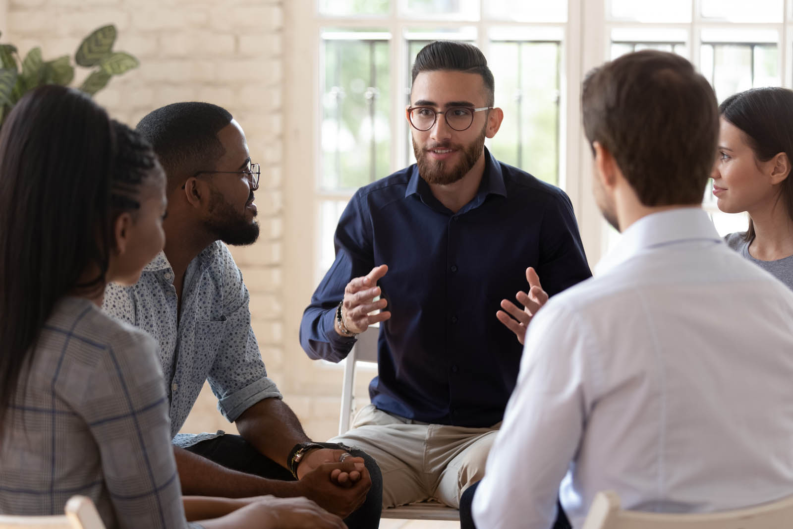 A diverse group of young adults sitting in a circle during a psychological group training session, engaged in conversation.