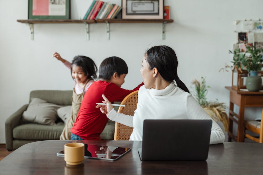 Young Asian working mother scolding little kids playing and making noise during remote job at home